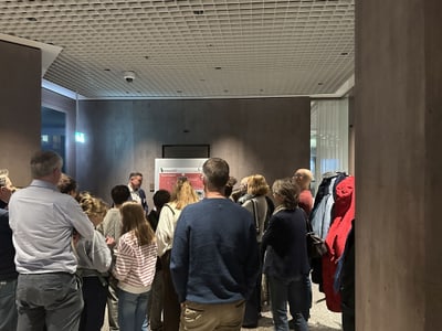 Gruppe von Menschen, die stehend eine Präsentation verfolgen.