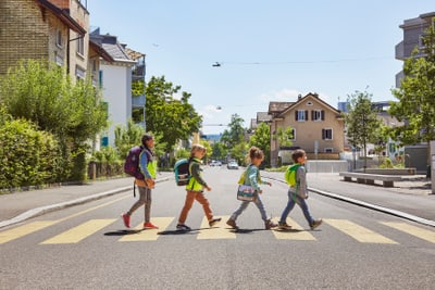 Kinder überqueren Zebrastreifen in Wohnviertel bei Sonne.