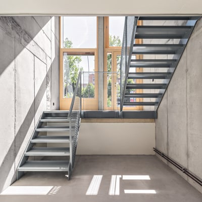 Moderne Metalltreppe in Betonraum mit grossen Fenstern.