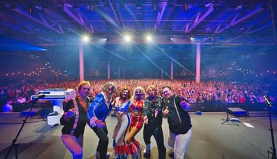 Band posing on stage in front of a large concert audience.