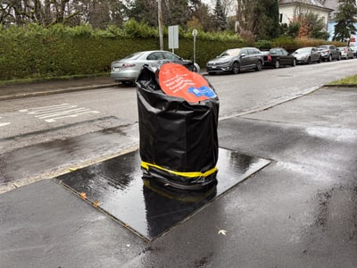 Grosser schwarzer Müllsack auf dem Bürgersteig neben Autos geparkt an der Strasse.