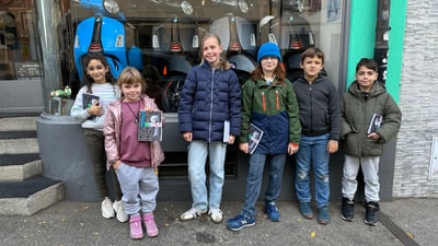 Sechs Kinder stehen vor einem Geschäft mit Rollern im Schaufenster.