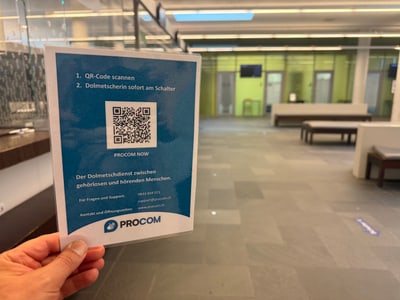 Hand hält einen Flyer in einem modernen Empfangsbereich.