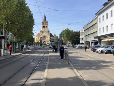 Strassenbahngleise mit einer Kirche im Hintergrund und Menschen auf der Strasse.