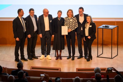 Personengruppe posiert auf Bühne mit Zertifikat.