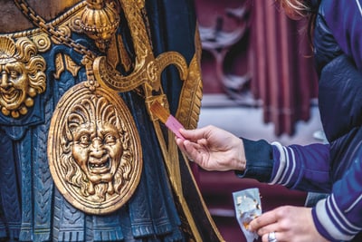 Person legt Karte in Schlitz einer dekorativen Rüstung.
