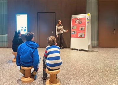 Frau präsentiert vor Publikum an Tafel im Innenraum.