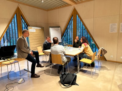 Besprechung in einem Raum mit fünf Personen an einem Tisch.