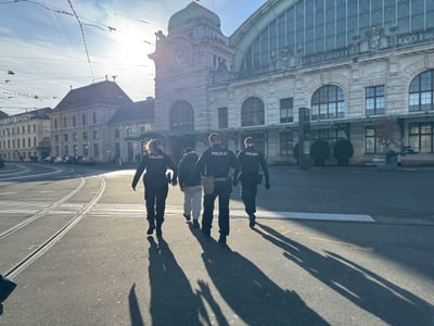 Polizisten begleiten Person vor grossem Bahnhofsgebäude bei Sonnenuntergang.