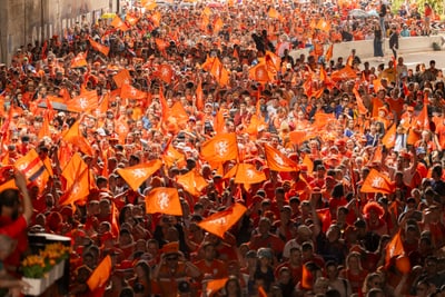 Menschenmenge mit orangefarbenen Fahnen bei einer Veranstaltung im Freien.