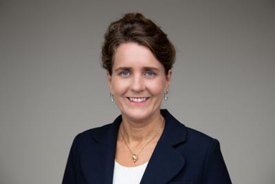 Frau in dunkelblazer vor neutralem Hintergrund.