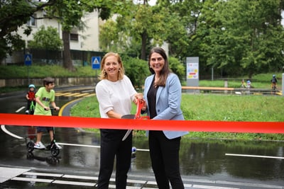 Zwei Frauen schneiden ein rotes Band bei einer Outdoor-Veranstaltung durch.
