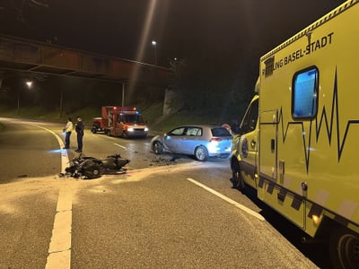 Unfallstelle bei Nacht mit Krankenwagen, Auto und Motorradtrümmern.",  