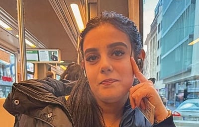 Frau sitzt im Zug und schaut in Richtung Kamera, Fenster im Hintergrund.