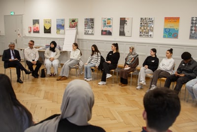 Gruppe Menschen in Stuhlkreis, Kunstwerke an der Wand im Hintergrund.