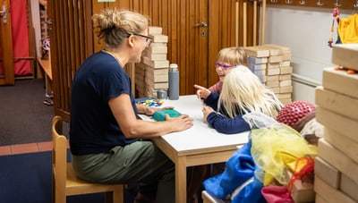 Erwachsener mit zwei Kindern an einem Tisch mit Bauklötzen.