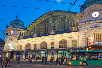 Beleuchtetes Bahnhofgebäude SBB am Abend mit Menschen und einem Bus davor.