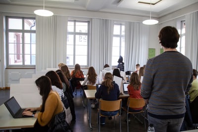 Klassenraum mit Schülern an Laptops und Lehrer.",