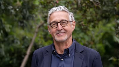 Älterer Mann mit Brille vor grünem Hintergrund.