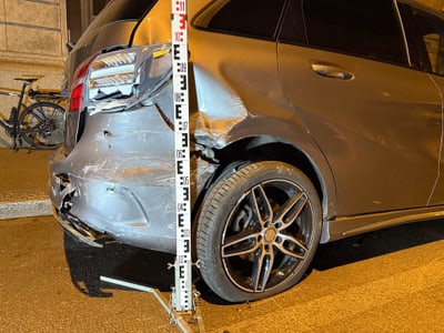 Beschädigtes Auto mit Messlatte und Fahrrad im Hintergrund bei Nacht.