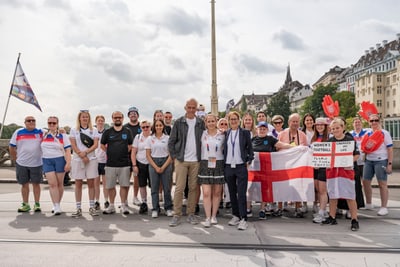 Gruppe von Menschen posiert mit Flagge auf einer Strasse in einer Stadt.