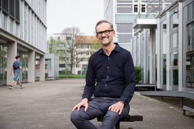 Peter Kalchofner sitzt draussen auf einer Bank vor einem Gebäude.