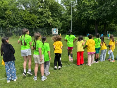 Kinder in bunten T-Shirts auf einem Sportplatz im Freien.