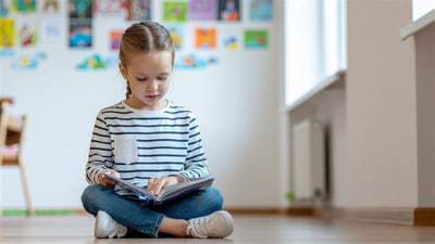 Mädchen liest Buch auf dem Boden sitzend.