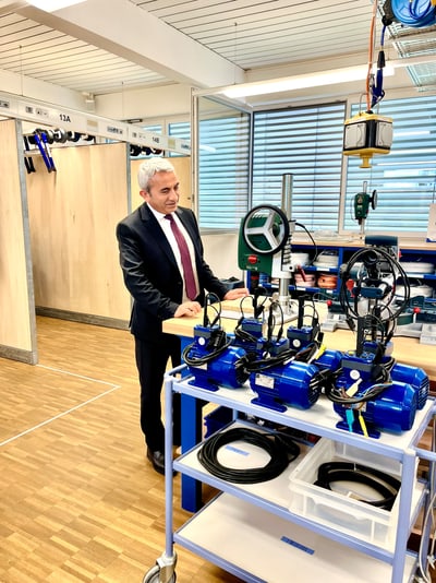 Departementsvorsteher Mustafa Atici in Anzug betrachtet Maschinen in Werkstatt.